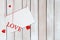 Paper postcard and word Love hanging on red threads surrounded by hearts with copy space on white wooden background