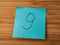 A paper sticker pasted on a wooden surface with the image of the number nine