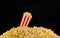 Paper striped bucket installed on scattered popcorn  on black background