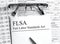 Paper with text FLSA on a financial table with eyeglasses and metal pen