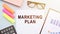 Paper with text marketing plan on table with colorful markers, glasses, financial graphs, calculator and notebook