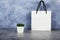 Paper white bag with a cup of coffee on a gray and blue background. Close up. Place for text. Mock up concept for gift wrapping.