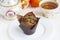 A paper-wrapped chocolate muffin on a white plate, a vintage sugar bowl and a cup of tea