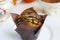 A paper-wrapped chocolate muffin on a white plate, a vintage sugar bowl and a cup of tea