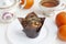 A paper-wrapped chocolate muffin on a white plate, a vintage sugar bowl, a cup of tea, and tangerines