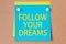 On a paperboard background - a light blue square sticker with the text follow your dreams, concept