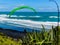 Para glider soars over the beach waves and hills at Murawai Beach Auckland New Zealand