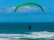 Para glider soars over the beach waves and hills at Murawai Beach Auckland New Zealand