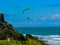 Para glider soars over the beach waves and hills at Murawai Beach Auckland New Zealand