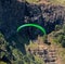 Para glider soars over the beach waves and hills at Murawai Beach Auckland New Zealand