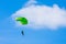 A parachutist with a light green parachute canopy against a background of blue sky and white clouds. Skydiving