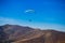 Paraglide silhouette flying over Carpathian peaks mountains on blue sky background.