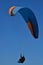 A paraglider drifts through a brilliant blue sky