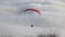 Paraglider flying over clouds with the mountains