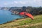Paraglider landing on a grassy hill in front of the ocean. Red paraglide open, no engine. Cliffs area by the sea. Asturias, North