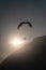 Paraglider over the silhouette of a wooded mountain ridge with the sun backlit