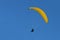 Paraglider pilot with a yellow glider is flying in the blue sky, recreational and competitive adventure sport, copy space