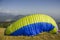 A Paraglider`s yellow blue parachute rises into the air before flying from the side of a hill against the background of a green
