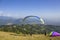 paraglider takes off on a blue parachute from a hillside against the background of a city in a green mountain valley