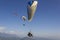 Paraglider on a white parachute flies against the background of other paragliders over a mountain valley in the fog under the blue