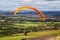 Paraglider with yellow parachute gliding over green landscape