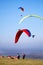 Paragliders in the sky, and on the ground with red and yellow ca