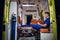 Paramedic in medical uniform sits with phone in his hands in the ambulance car at night