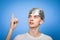 Paranoid young man wearing tin foil hat pointing up studio shot on blue background