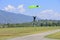 paratrooper with green parachute prepares for landing. On background the blue sky, mountains and green hills