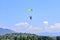 paratrooper with green parachute prepares for landing. On background the blue sky, mountains and green hills