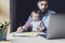 Parent with child studying remotely at homebased laptop. Distant education for people with babies.Man and toddler sitting at table