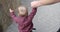 Parent helps child to take first steps on asphalt on open air, mother supports her little baby