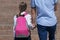 Parent leads by daughter`s hand to school, close-up view from behind