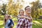 Parents carry kids piggyback in park, dad and girl in front