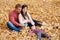 Parents and child are sitting in autumn city park. Bright yellow trees