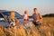 Parents and child sitting on car cowl on wheaten f