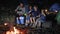 Parents with children puts zephyr to skewer near campfire in woodland, family communicates and putting marshmallows