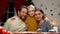 Parents and girl looking to camera, Xmas tree sparkling behind, family portrait