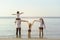 Parents are holding hands their children and walking on the beach at sunset in holiday