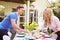 Parents Putting Food On Table For Childrens Outdoor Easter Party In Garden At Home