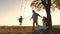 Parents swing a happy child high up on a swing at sunset, a cheerful family in the glare of the sun plays with their