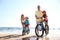 Parents teaching children to ride bicycles on sandy beach near sea