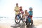 Parents teaching children to ride bicycles on sandy beach near sea