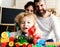 Parents watch son with funny face making brick constructions.