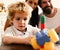 Parents watch their son with busy face making brick constructions