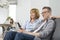 Parents watching TV on sofa with children using laptop in background