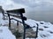 Park bench atop a snow-covered shore overlooking a serene ocean