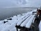 Park bench atop a snow-covered shore overlooking a serene ocean