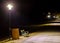 Park bench and trash container illuminated by a lantern