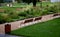 Park benches lined with wood along the entire wide threshing gravel beige path, lawns, flower lush, perennial flower beds blooming